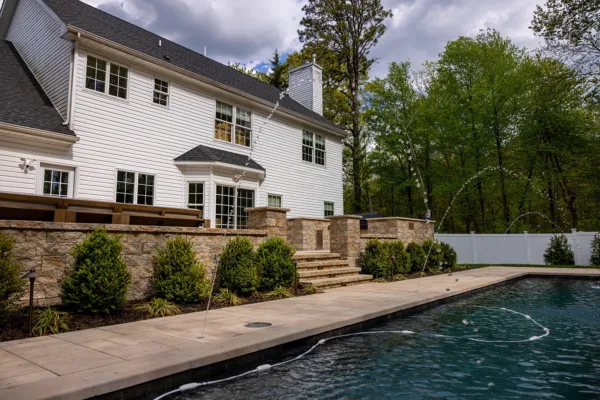 This Old Bridge, NJ backyard was transformed into a luxurious outdoor retreat featuring a raised patio and pool deck, outdoor kitchen, custom pavilion, water features, landscape lighting, fresh sod, and professional landscaping. The design combines durability and elegance, with a fully equipped outdoor kitchen, a shaded pavilion for entertaining, and stunning water features that enhance the space. With low-voltage LED lighting and lush greenery, this backyard is now perfect for both relaxation and hosting.